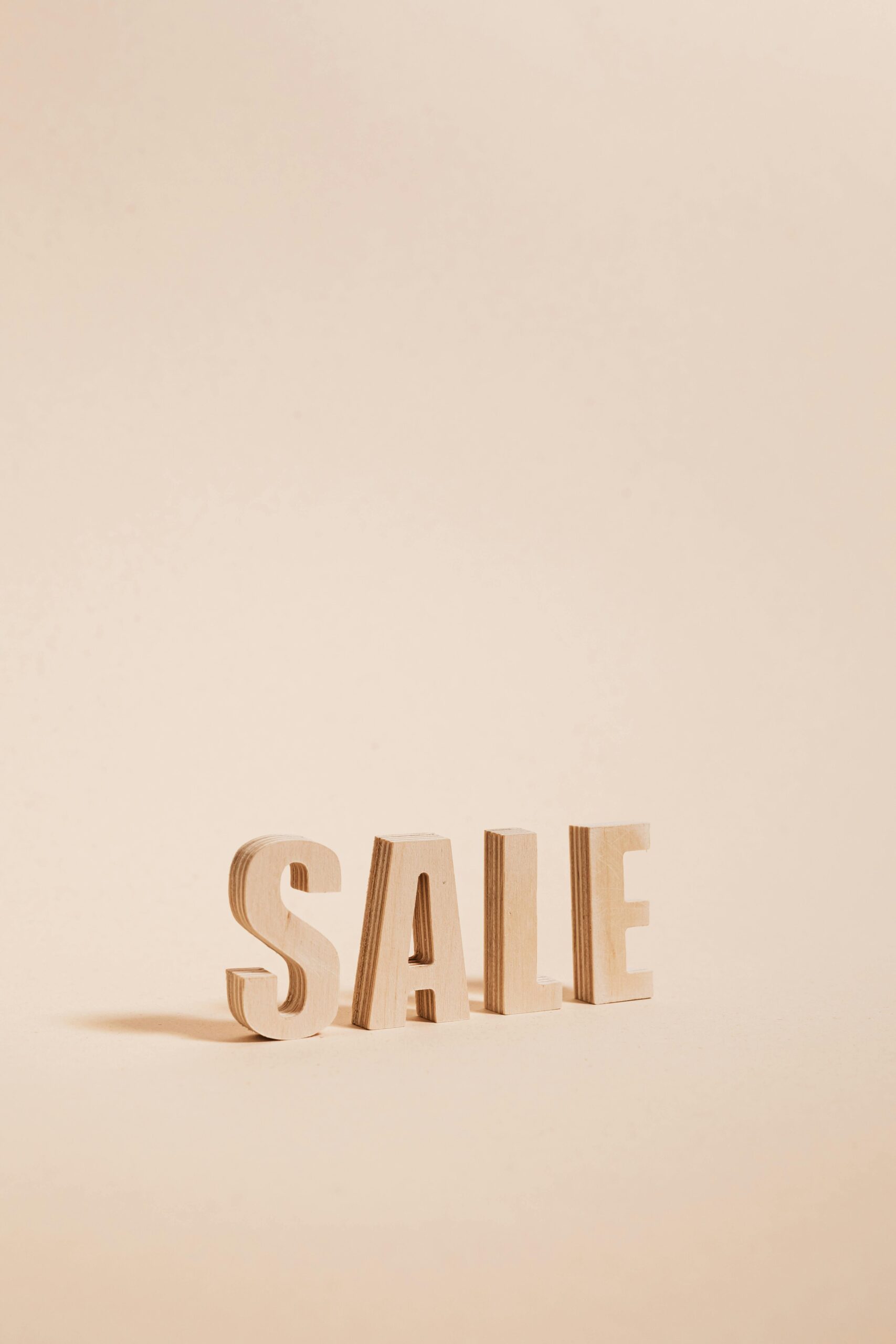 Wooden letters spelling SALE on a neutral beige background, perfect for promotions.